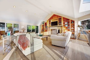 A spacious living room with a fireplace, a large bookshelf, and a painting on the wall. - Gualala 2BR oceanfront blufftop home with hot tub — sleeps 4 (Gualala)