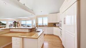 A modern kitchen with white cabinetry, a large island, and a view of the sea. - Gualala 2BR oceanfront blufftop home with hot tub — sleeps 4 (Gualala)