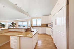 A modern kitchen with white cabinetry, a large island, and a view of the sea. - Gualala 2BR oceanfront blufftop home with hot tub — sleeps 4 (Gualala)