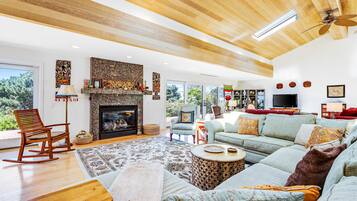 A spacious living room with a fireplace, wooden ceiling, and large windows.
