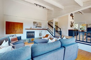 A spacious living area with a large gray sofa set, a wooden cabinet, and a staircase leading to another level. - Sea Ranch 3BR luxe home with hot tub, ocean glimpses & yoga space (Sea Ranch)