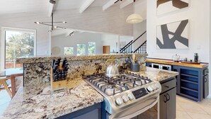 Een keuken met een gasfornuis, een granieten aanrechtblad en moderne hanglampen.