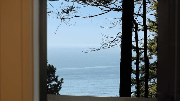 A view through a window with a railing, overlooking a body of water and trees. - Sea Ranch 3BR home with deck & grill near Shell Beach — dogs welcome (Sea Ranch)