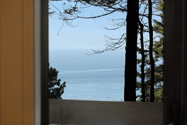 A view through a window with a railing, overlooking a body of water and trees. - Sea Ranch home with deck & grill near Shell Beach, dogs welcome (Sea Ranch)
