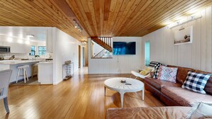 A modern interior with a wooden ceiling, a kitchen with white cabinets, a dining area with a white table, and a brown leather sofa with patterned cushions. - Sea Ranch 3BR home with deck & grill near Shell Beach — dogs welcome (Sea Ranch)