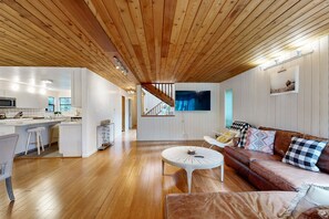 A modern interior with a wooden ceiling, a kitchen with white cabinets, a dining area with a white table, and a brown leather sofa with patterned cushions. - Sea Ranch home with deck & grill near Shell Beach, dogs welcome (Sea Ranch)