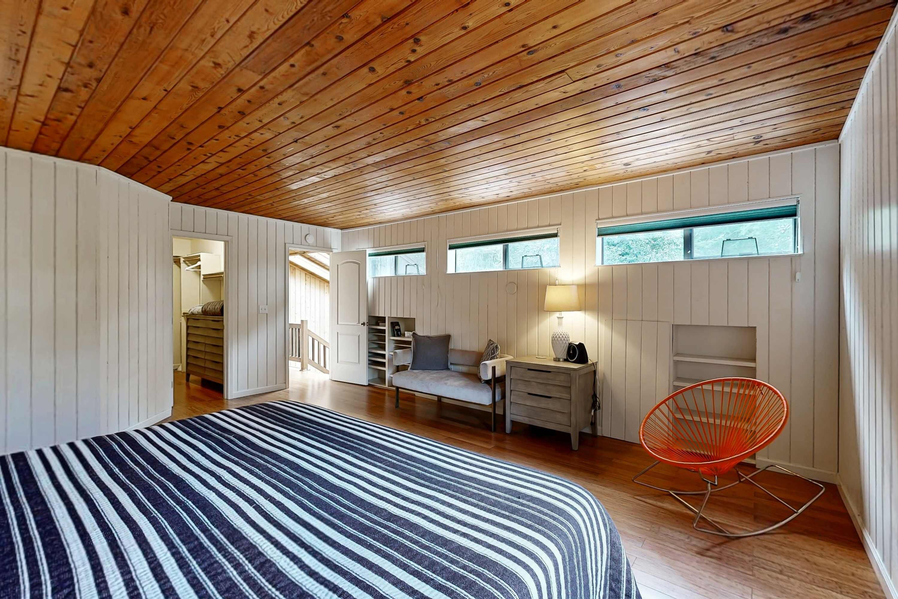 A bedroom with a bed, a rocking chair, a desk, and built-in shelving.