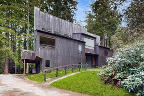 A modern wooden house with a staircase leading to the entrance, surrounded by a forest. - Sea Ranch home with deck & grill near Shell Beach, dogs welcome (Sea Ranch)