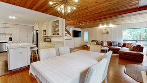 A modern interior with a wooden ceiling, a central bed, a sofa, a dining area, and a kitchen. - Sea Ranch 3BR home with deck & grill near Shell Beach — dogs welcome (Sea Ranch)