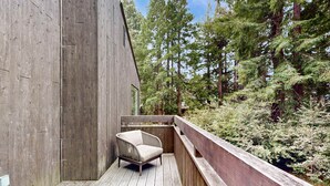 A wooden deck with a chair, surrounded by a wooden railing, and a forested backdrop. - Sea Ranch 3BR home with deck & grill near Shell Beach — dogs welcome (Sea Ranch)