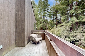 A wooden deck with a chair, surrounded by a wooden railing, and a forested backdrop. - Sea Ranch home with deck & grill near Shell Beach, dogs welcome (Sea Ranch)