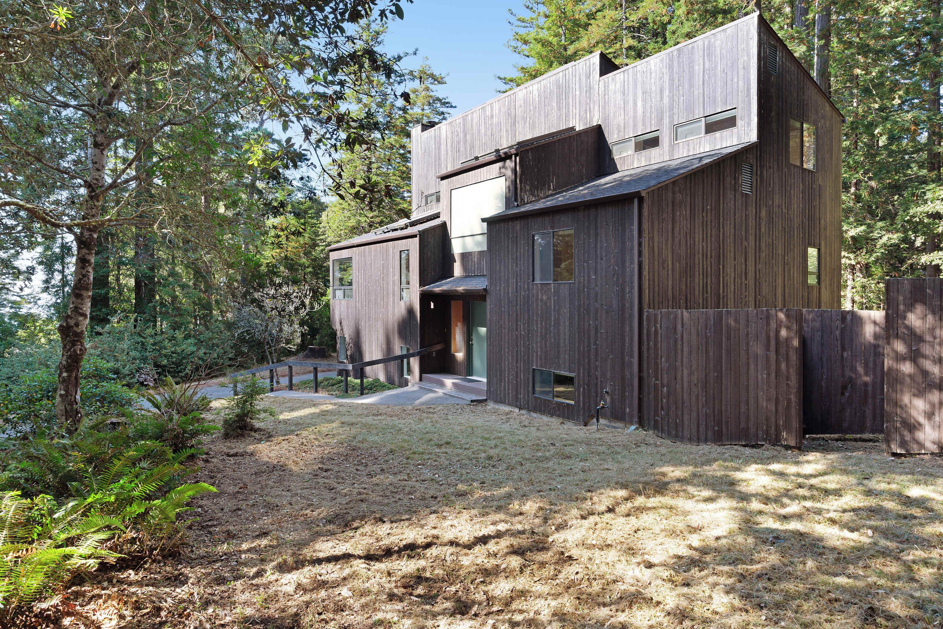 A modern wooden building with a flat roof, large windows, and a pathway leading to the entrance.