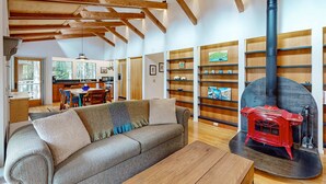 A cozy living room with a sofa, a wooden table, and a red wood-burning stove. - Sea Ranch 2BR forested home with deck & grill near the Lodge — dog friendly (Sea Ranch)