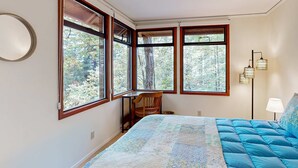 A bedroom with a large bed, a desk, and multiple windows. - Sea Ranch 2BR forested home with deck & grill near the Lodge — dog friendly (Sea Ranch)
