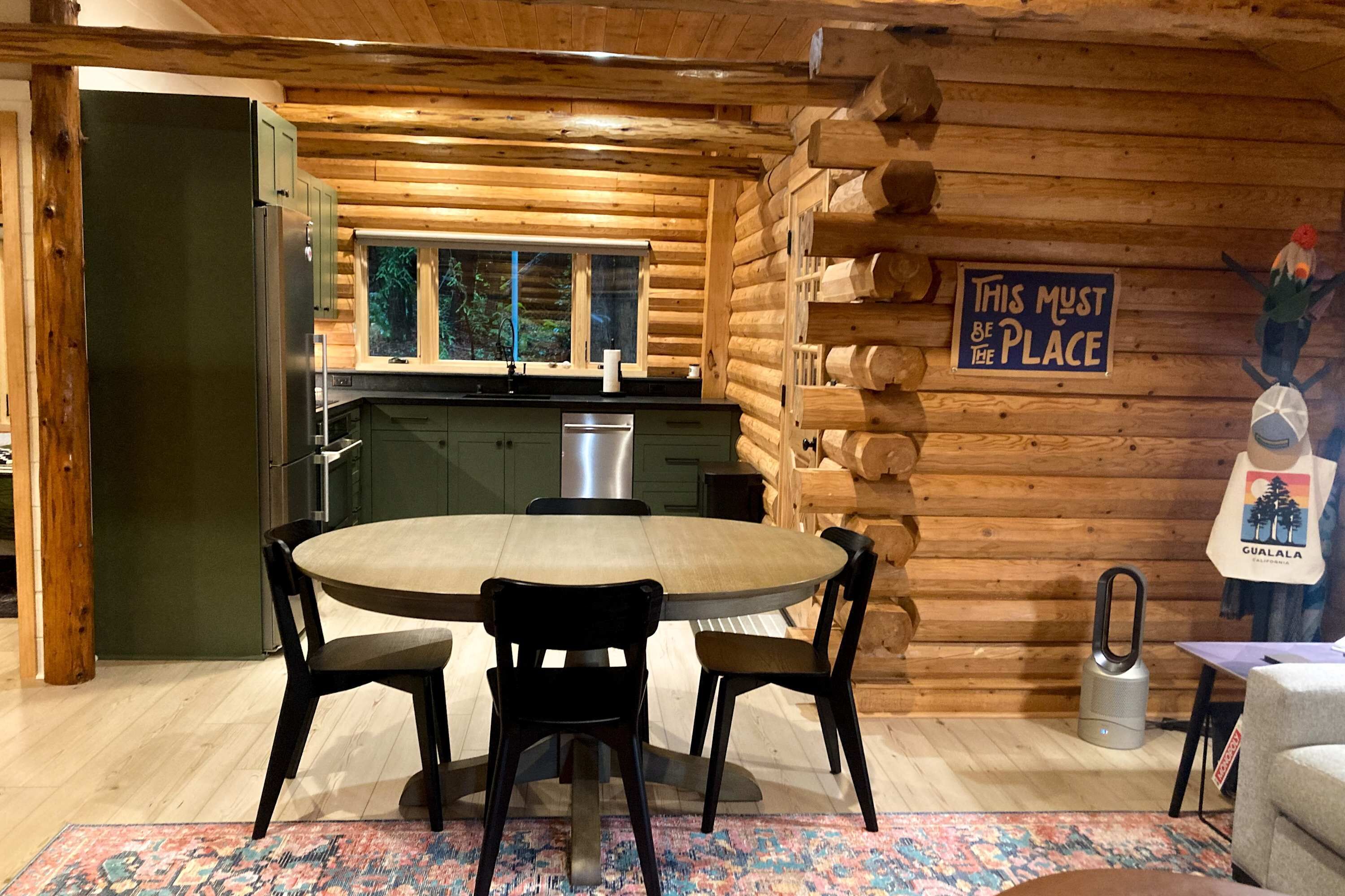 A log cabin interior with a dining area, kitchen, and a sign on the wall.