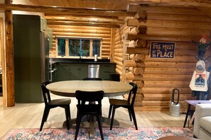 A log cabin interior with a dining area, kitchen, and a sign on the wall. - Gualala 2BR log cabin in the redwoods — fire-table deck & EV charger (Gualala)