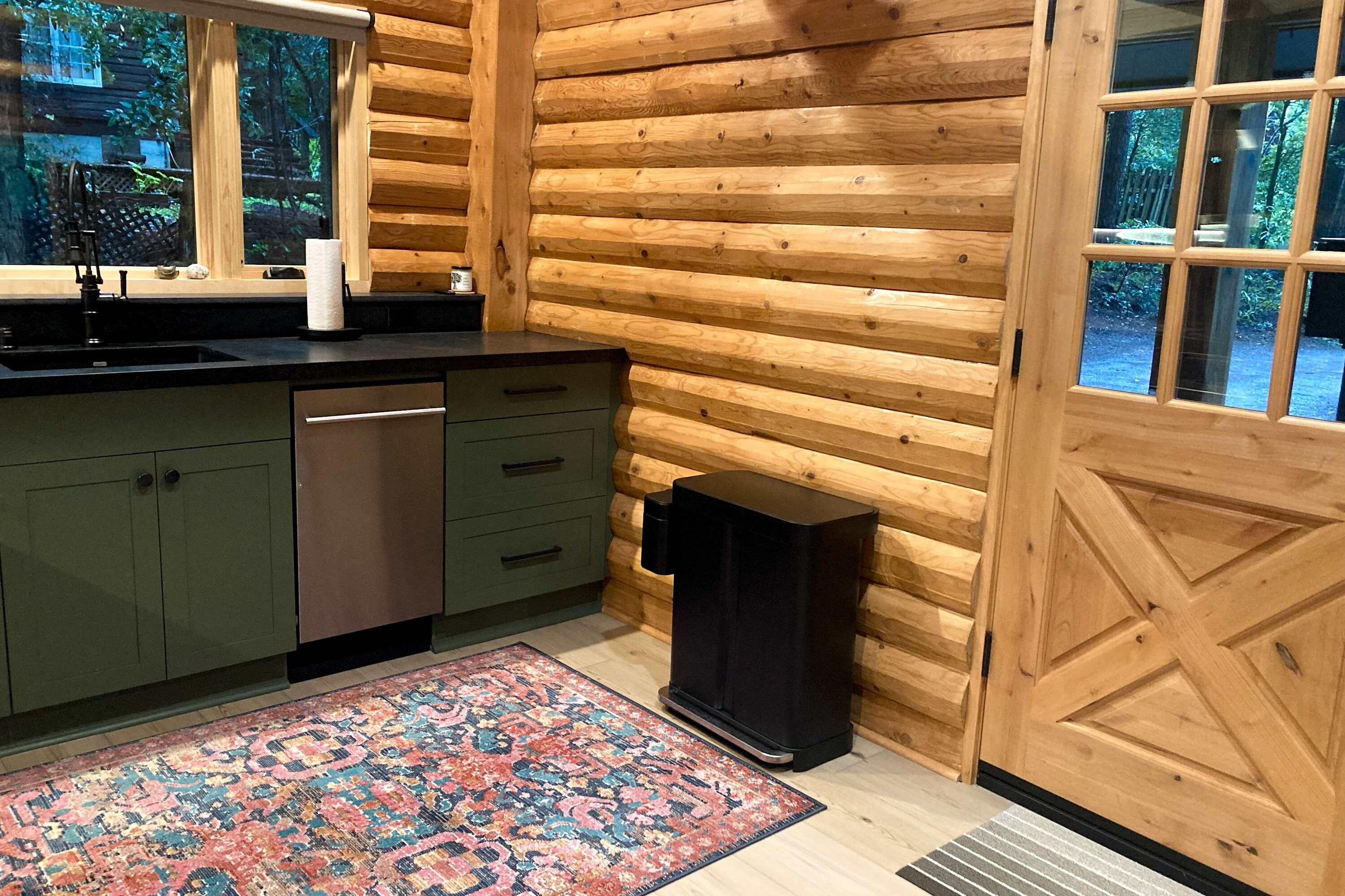 A log cabin interior with a kitchen area, including a sink, cabinets, a rug, and a speaker.