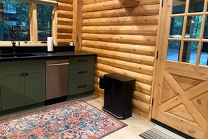 A log cabin interior with a kitchen area, including a sink, cabinets, a rug, and a speaker. - Gualala 2BR log cabin in the redwoods — fire-table deck & EV charger (Gualala)
