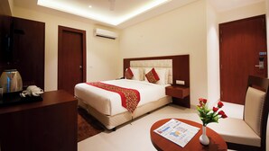 A hotel room with a bed, a desk, a chair, a vase with flowers, and a ceiling fan. - Z Premium Suites -Near IGI Delhi Airport (New Delhi)