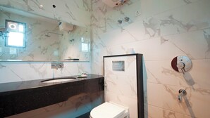 A modern bathroom with a marble backsplash, a black countertop sink, a white toilet, and a glass-enclosed shower area. - Z Premium Suites -Near IGI Delhi Airport (New Delhi)