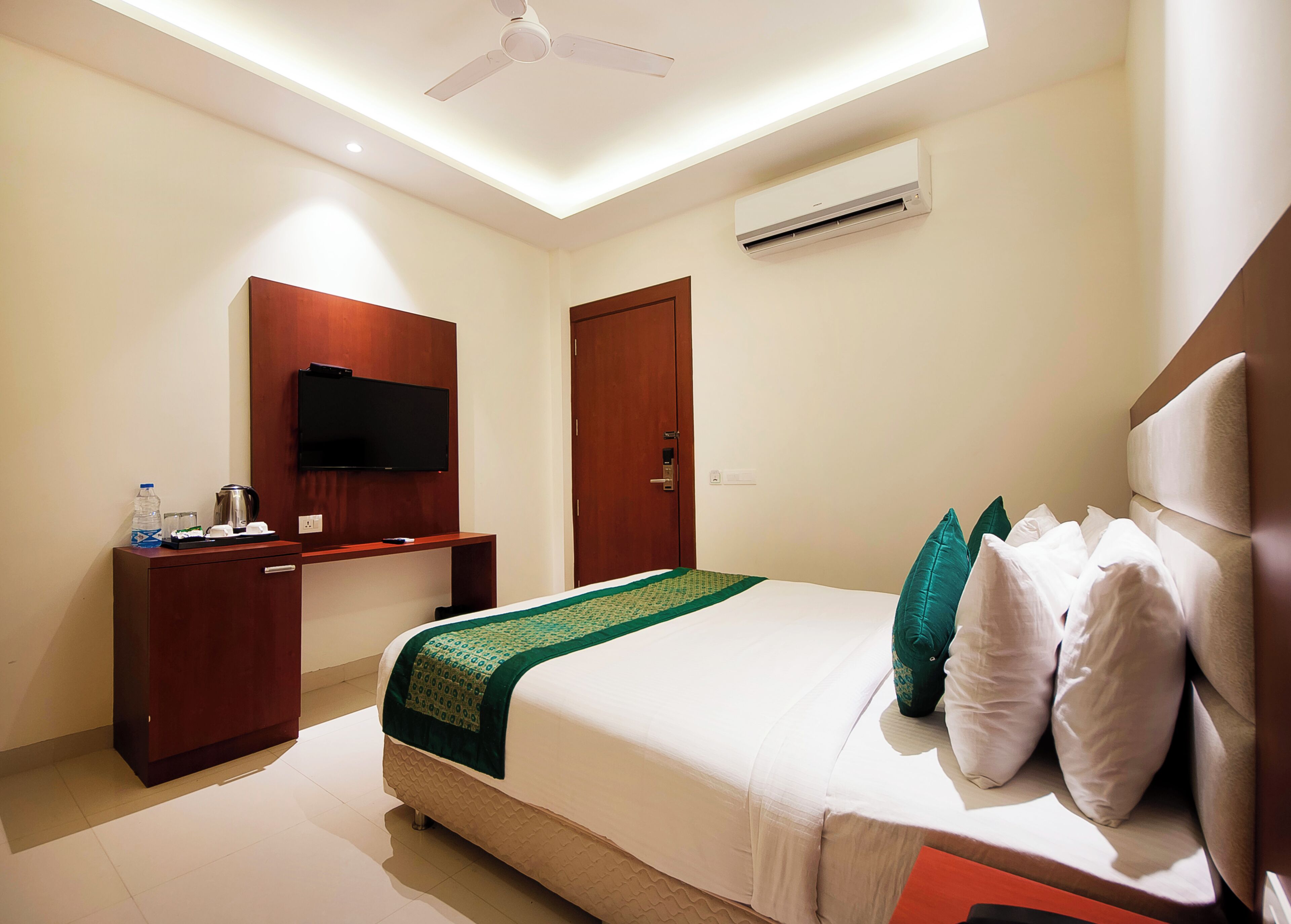 A hotel room with a bed, a desk, a television, and an air conditioning unit.