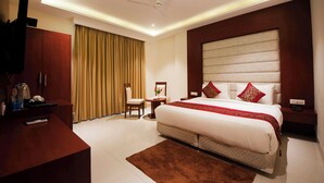 A hotel room with a large bed, a desk, a chair, a TV, and a ceiling fan. - Z Premium Suites -Near IGI Delhi Airport (New Delhi)
