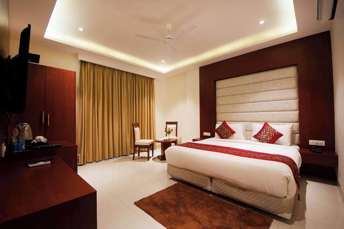 A hotel room with a large bed, a desk, a chair, a TV, and a ceiling fan.