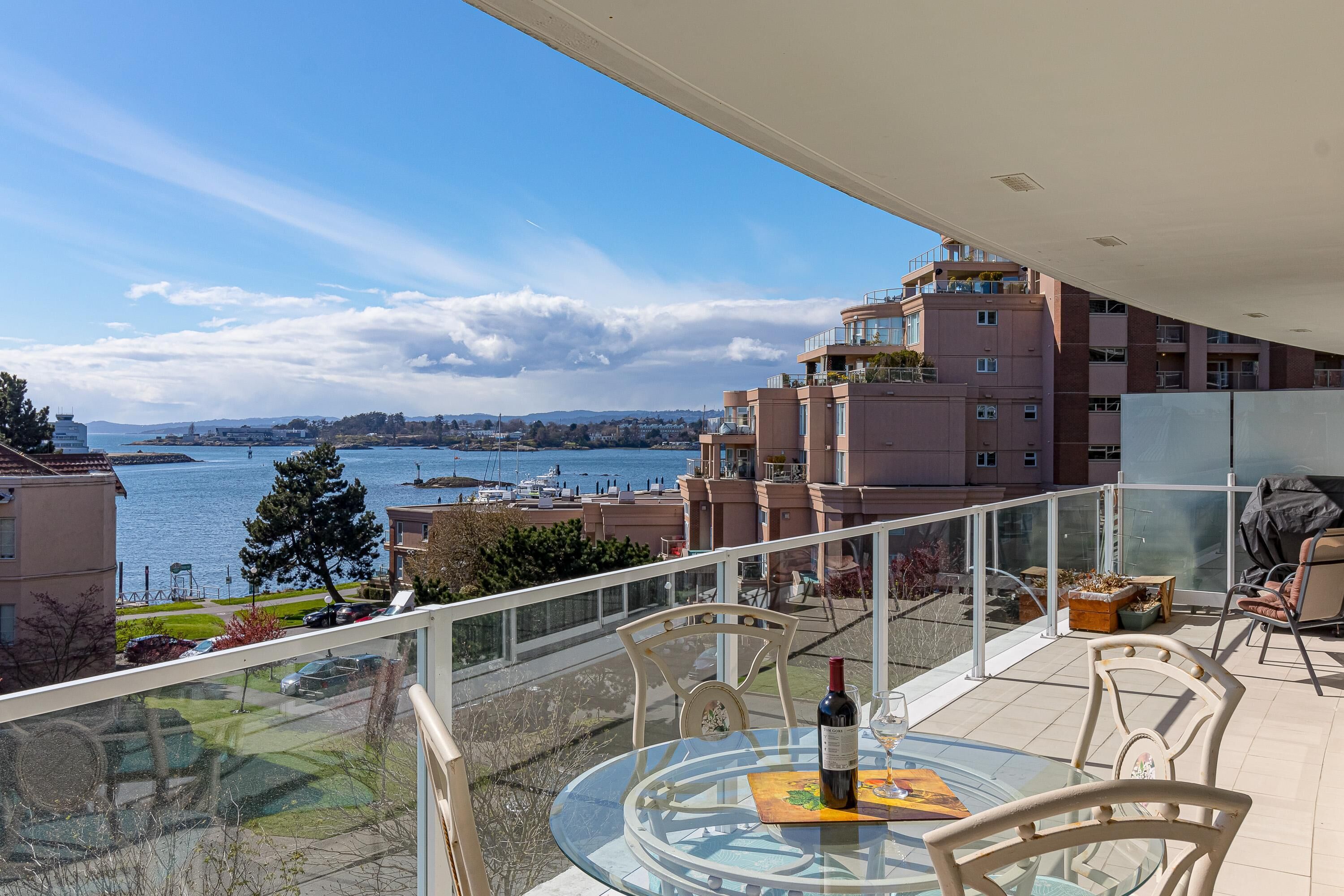 A balcony with a glass table, chairs, and a bottle of wine.