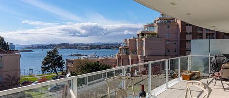 A balcony with a glass table, chairs, and a bottle of wine.