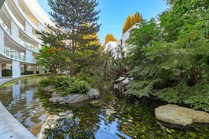 Ein modernes Gebäude mit einem Innenhof, der einen Teich, Felsen und viel Grünwerk aufweist.