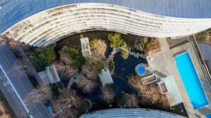 Um edifício moderno com telhado curvo, piscina e área de jardim ajardinado.