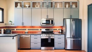 Een moderne keuken met een magnetron, oven, koelkast en een kastje met decoratieve voorwerpen.