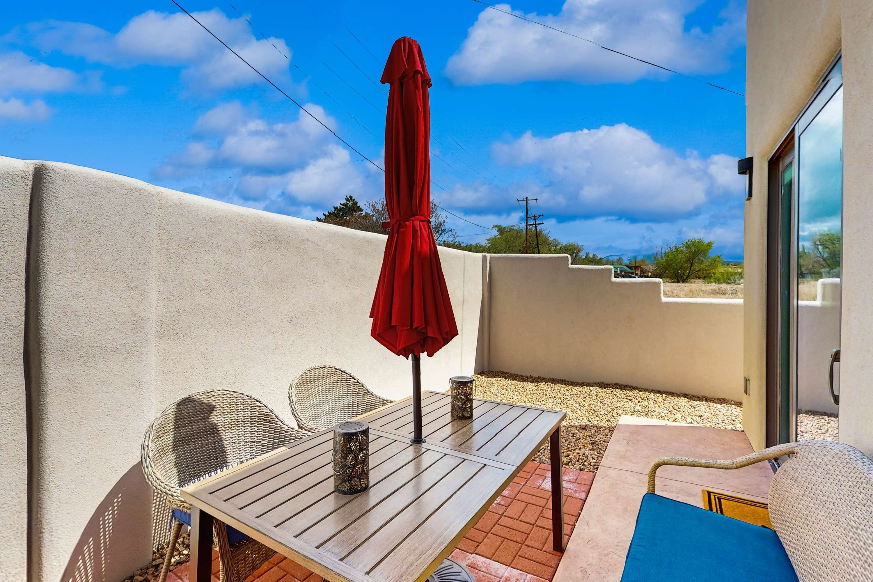 A patio with a table and chairs, a red umbrella, and a view of the sky.