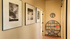 Een hal met aan de muur ingelijste foto's, een deur en een boekenkast vol boeken en spellen.