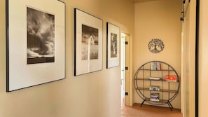 Ein Flur mit gerahmten Bildern an der Wand, einer Tür und einem Bücherregal mit Büchern und Spielen.