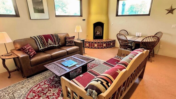Een woonkamer met een open haard, een bank, een salontafel en een eethoek met stoelen.