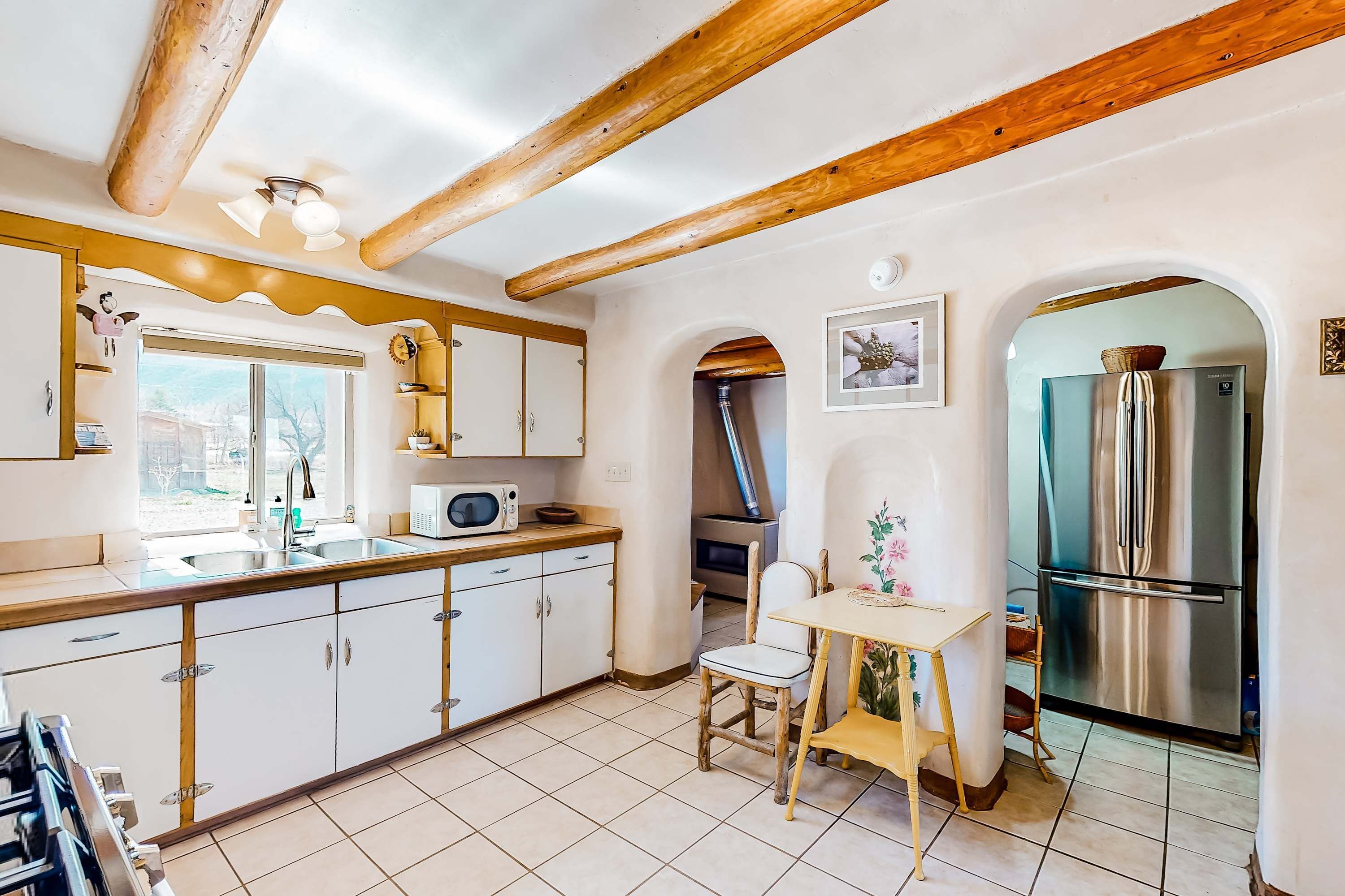 A kitchen with white cabinets, a wooden ceiling, a stainless steel refrigerator, and a window.