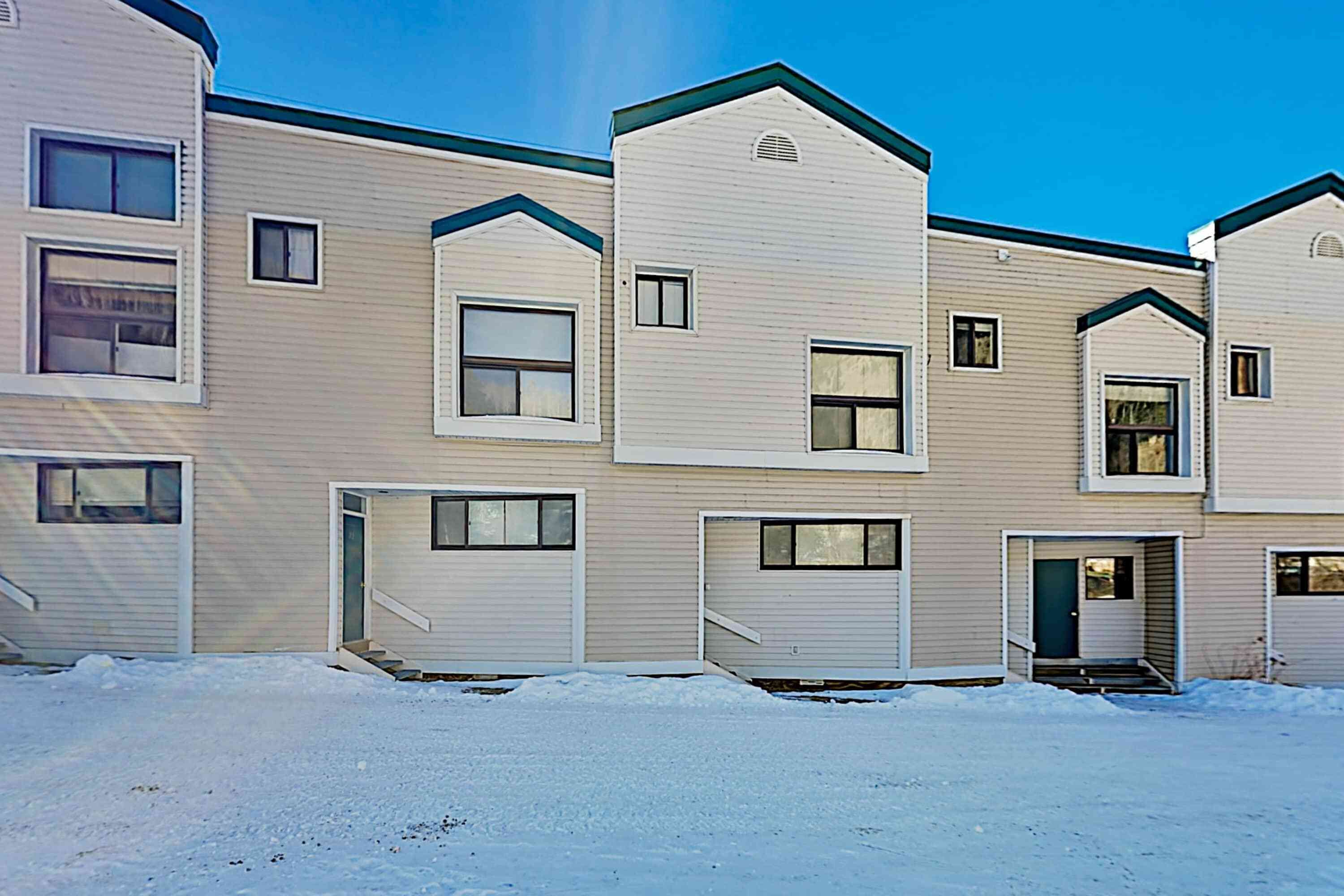 A multi-story residential building with a flat roof, multiple windows, and a snow-covered ground.