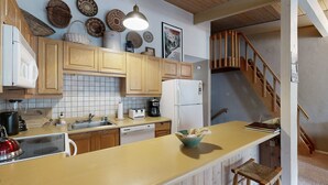 A kitchen with wooden cabinets, a countertop, a sink, a refrigerator, and a wooden staircase. - Sierra Del Sol 30 - Hot Tub, Walk to Lifts & Town (Taos Ski Valley)