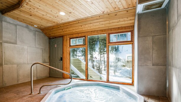 A hot tub with a wooden interior, a metal ladder, and large windows offering a view of a snowy landscape. - Sierra Del Sol 30 - Hot Tub, Walk to Lifts & Town (Taos Ski Valley)