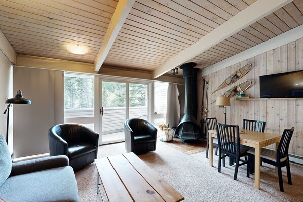 A cozy living room with a wooden ceiling, a fireplace, a TV, and a dining area.