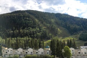 Un hotel con una hilera de edificios, una montaña boscosa al fondo y un cielo despejado.