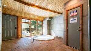 A spa room with a wooden ceiling, a hot tub, and a door with a warning sign. - Sierra Del Sol 30 - Hot Tub, Walk to Lifts & Town (Taos Ski Valley)