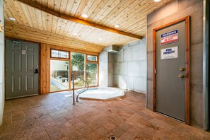 A spa room with a wooden ceiling, a hot tub, and a door with a warning sign.
