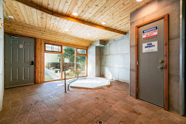 A spa room with a wooden ceiling, a hot tub, and a door with a warning sign.
