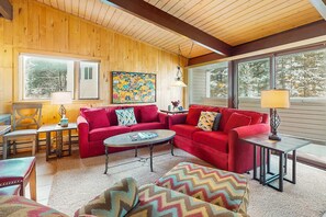 Un salón acogedor con un sofá rojo, una mesa de centro redonda y techo de madera.