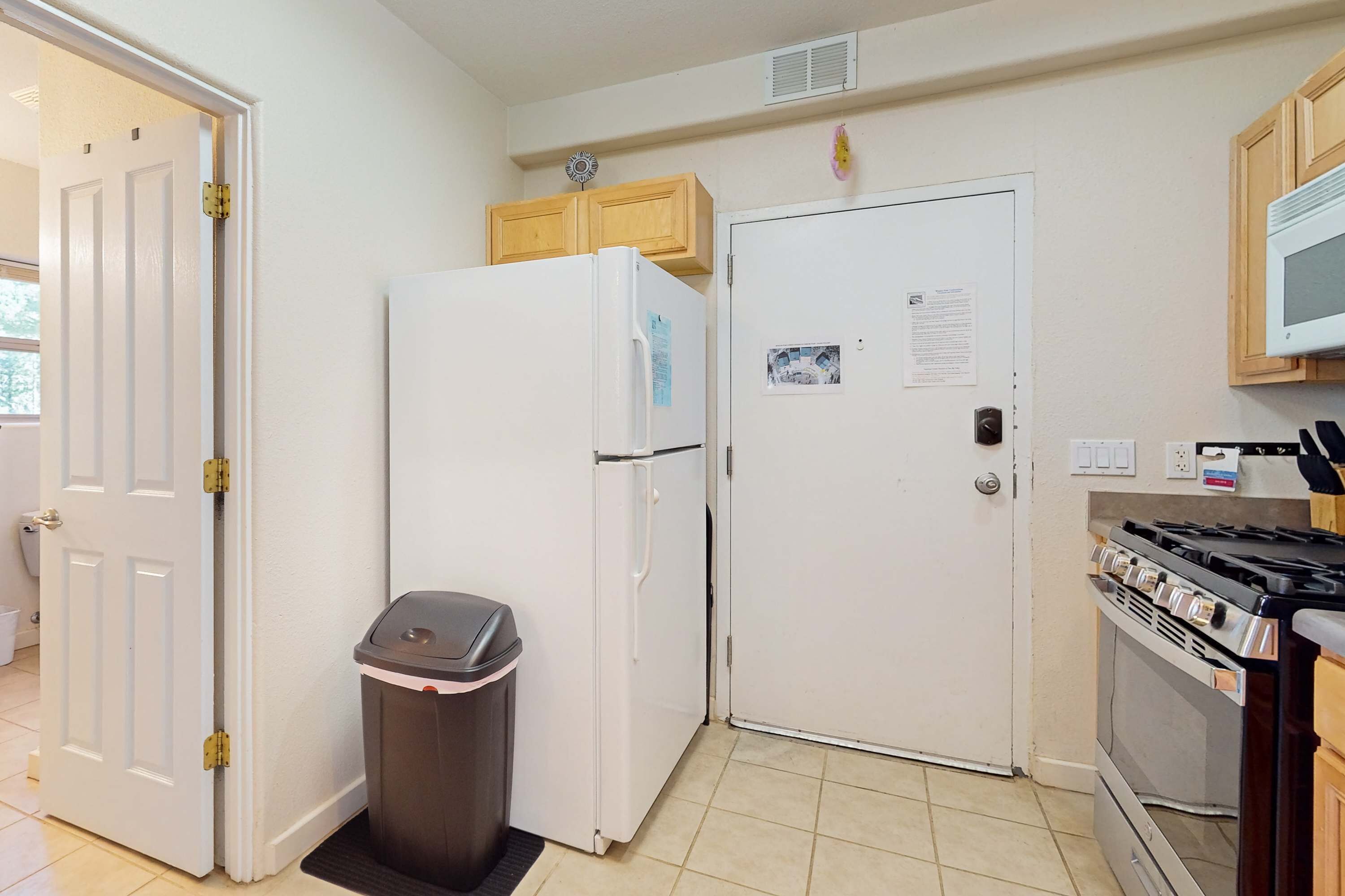A kitchen with a refrigerator, stove, and trash bin.