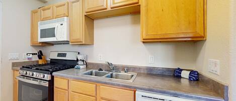 Una cocina con gabinetes de madera, estufa de acero inoxidable, microondas, lavavajillas y un lavamanos doble.