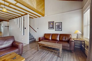 A living room with a brown leather sofa, a wooden coffee table, and a staircase leading to another level. - Timbers Five - Walk to Ski, Hike, Bike & Dining (Angel Fire)