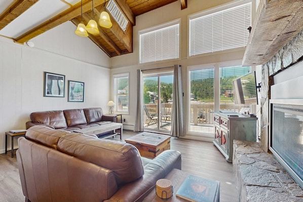 A spacious living room with a leather sofa, a wooden coffee table, and a fireplace. - Timbers Five - Walk to Ski, Hike, Bike & Dining (Angel Fire)